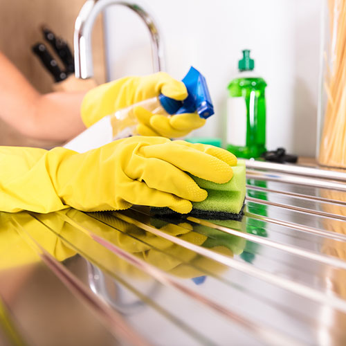 Gloved hands scrubbing a stainless steel sink